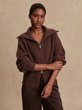 Woman wearing a brown ribbed knit zip-up jacket with a wide collar and matching brown pants standing against a beige background