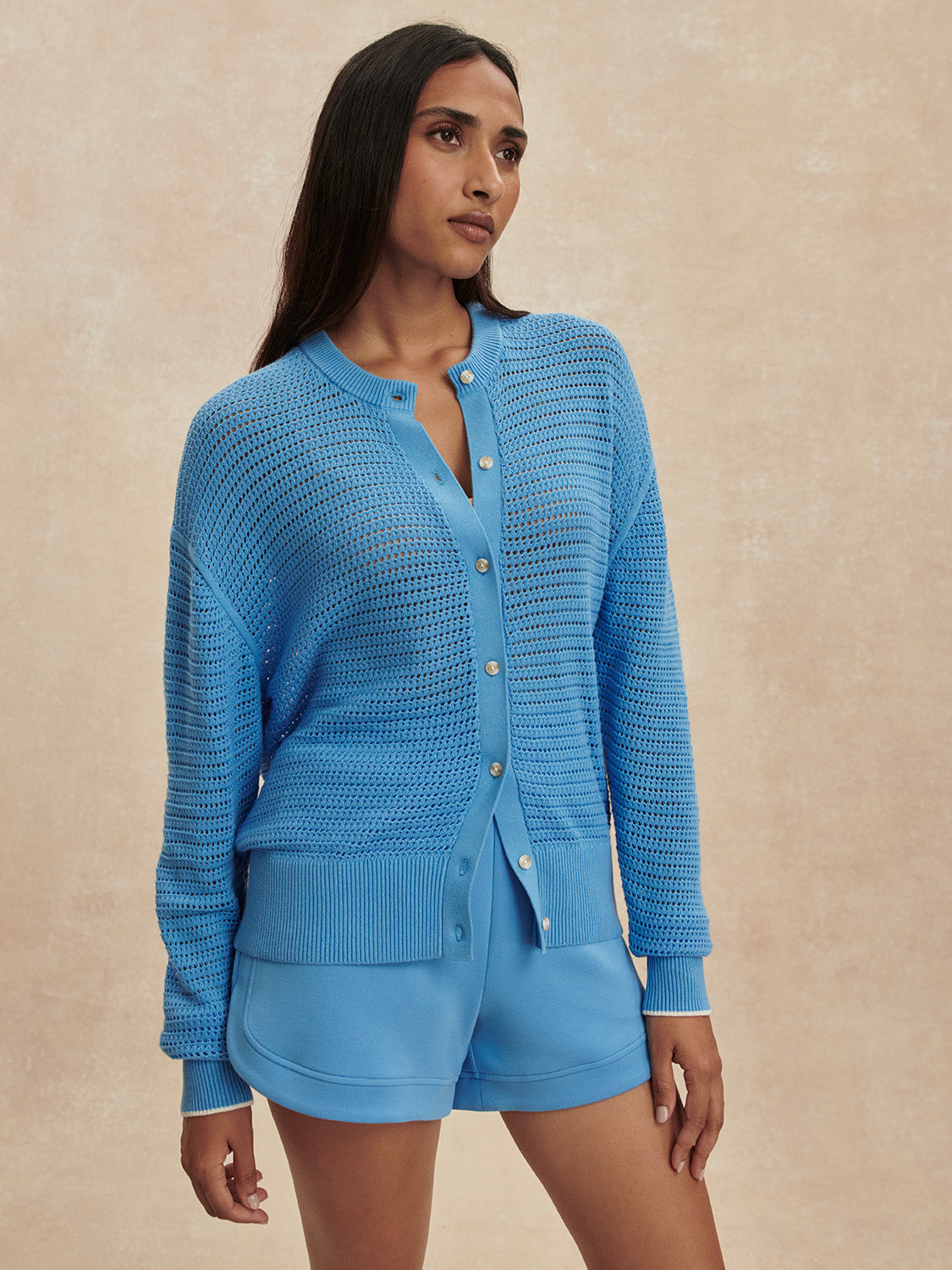 Woman wearing an Azure Blue Pembroke Knit Cardigan by Varley with matching shorts against neutral background