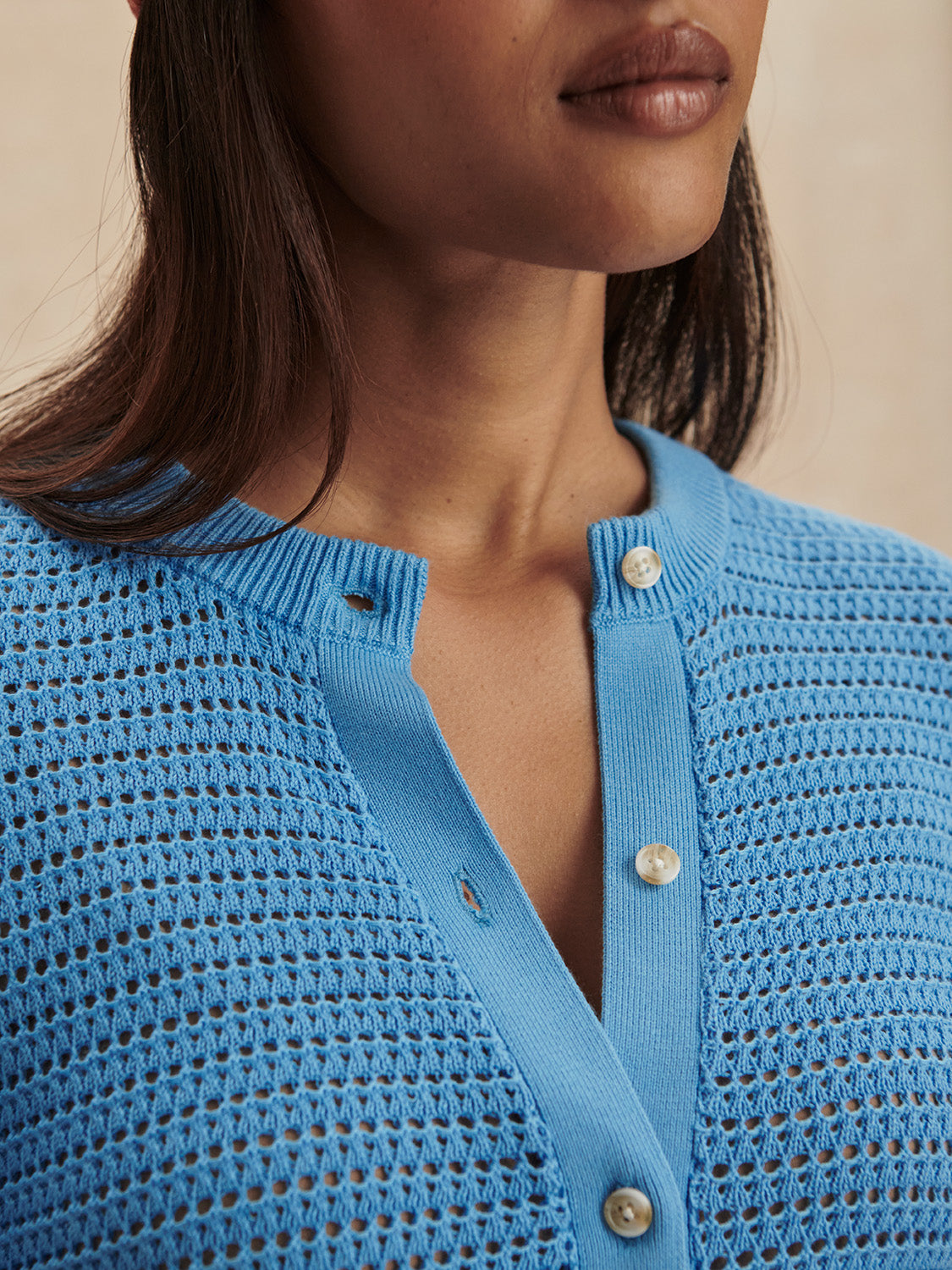 Close-up of a woman wearing an Azure Blue Pembroke Knit Cardigan by Varley with pearl buttons and textured knit pattern