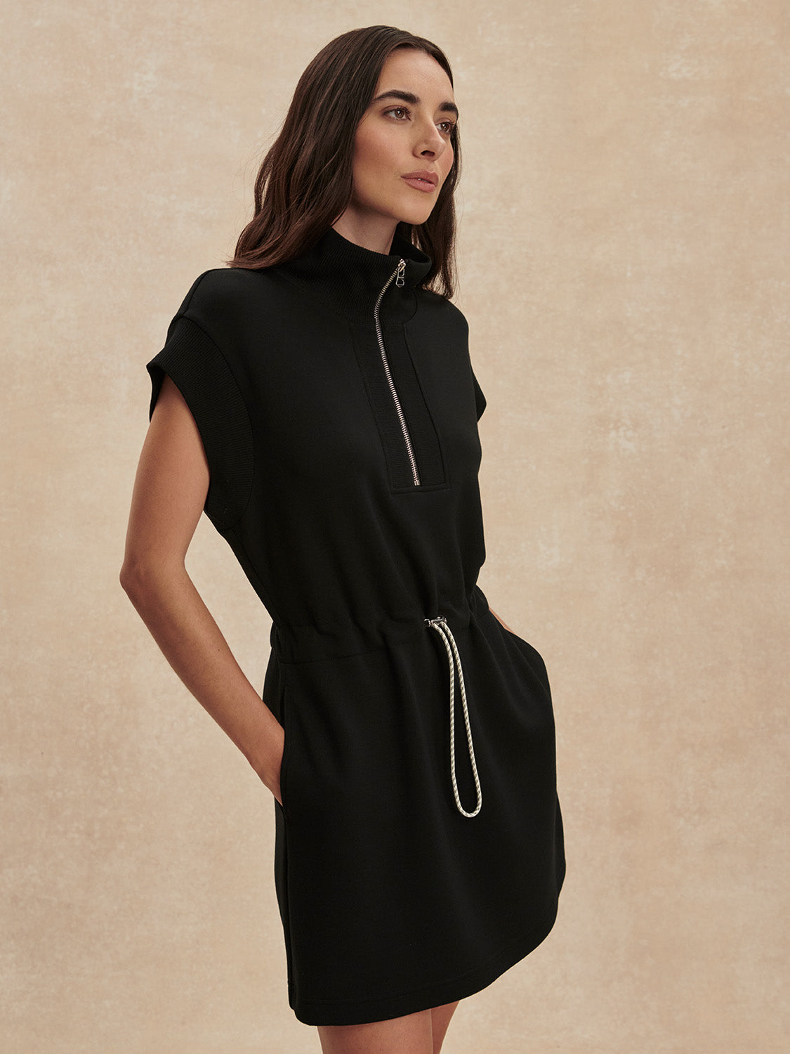 Woman wearing a sleek Black Avaya Half Zip Dress by Varley with a stand collar and drawstring waist details.