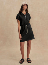Woman wearing a black Black Avaya Half Zip Dress by Varley with a rope belt and a beige cap in a neutral setting