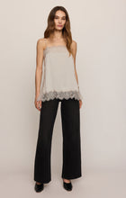 Woman wearing a beige lace-trim camisole with black wide-leg pants against a neutral background