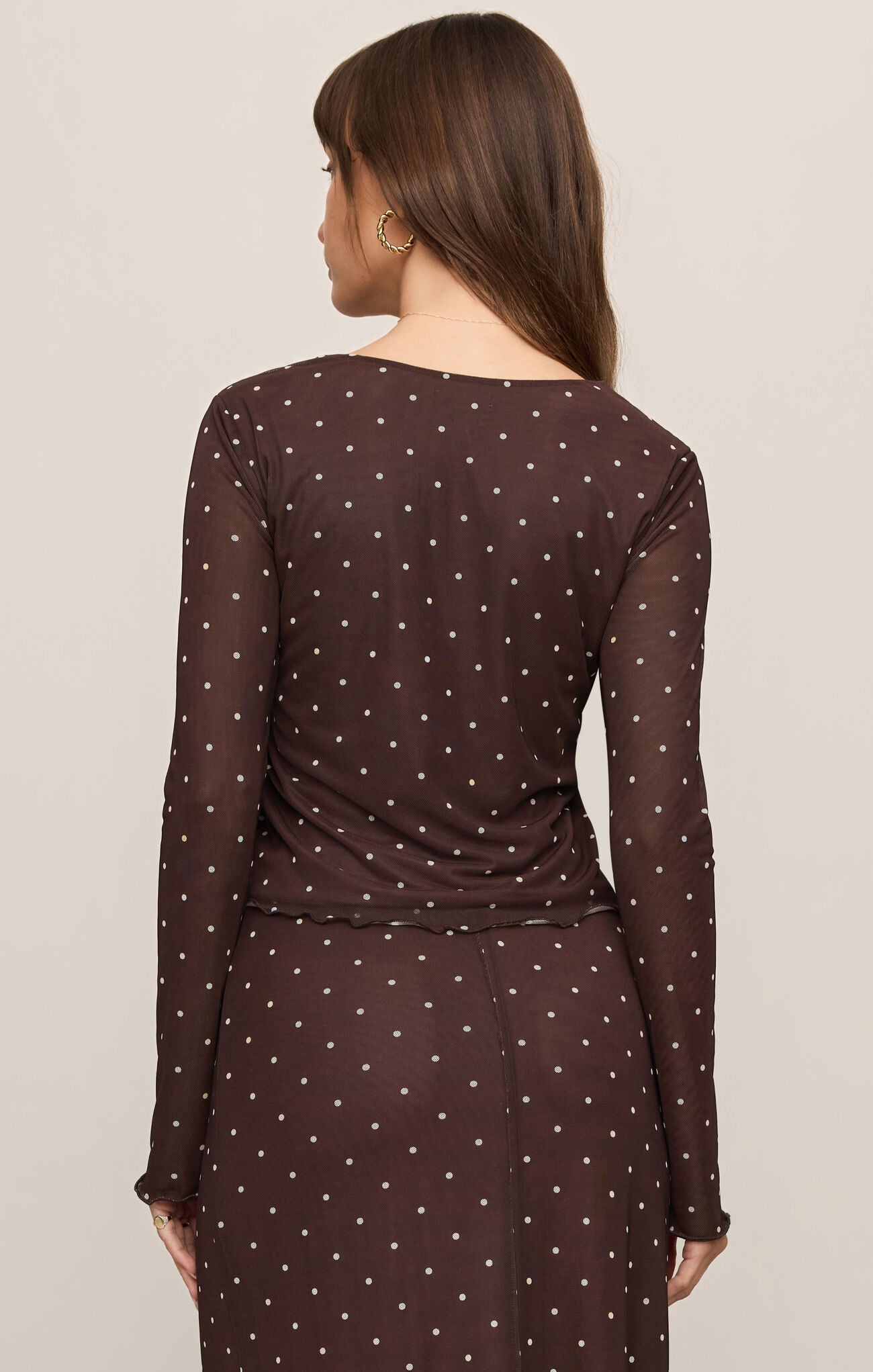 Woman wearing a sheer Dark Chocolate Amara Polka Dot Mesh Top by z supply, shown from the back with long sleeves