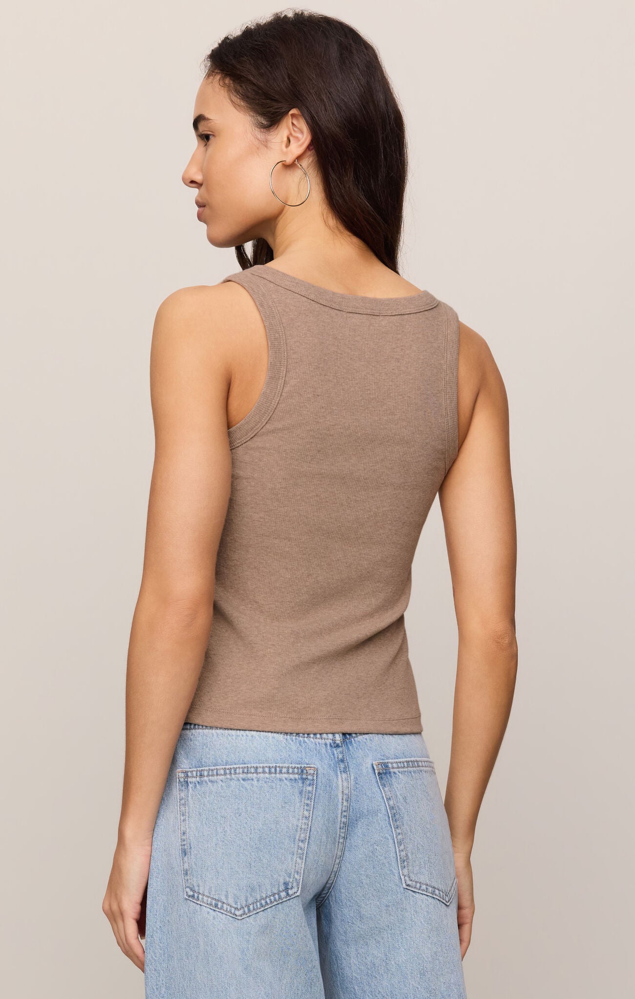 Woman wearing a taupe Rowe Scoop Tank by z supply paired with light blue denim jeans, shown from the back view.