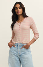 Woman with dark hair wearing a washed pink striped henley top and light blue jeans standing with hands in pockets
