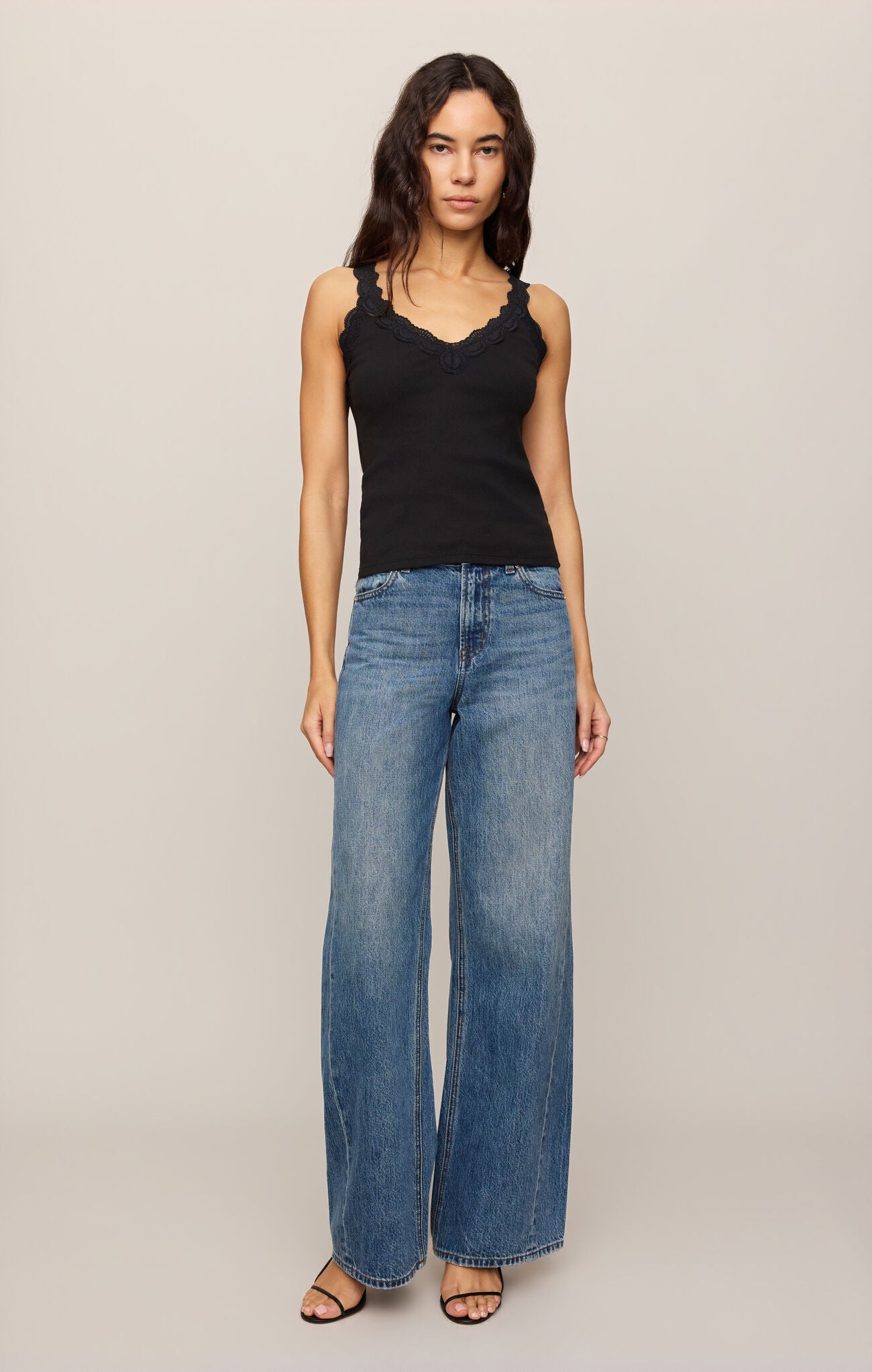 Woman wearing a Black Eve Lace Tank by z supply paired with wide-leg blue jeans and black sandals.
